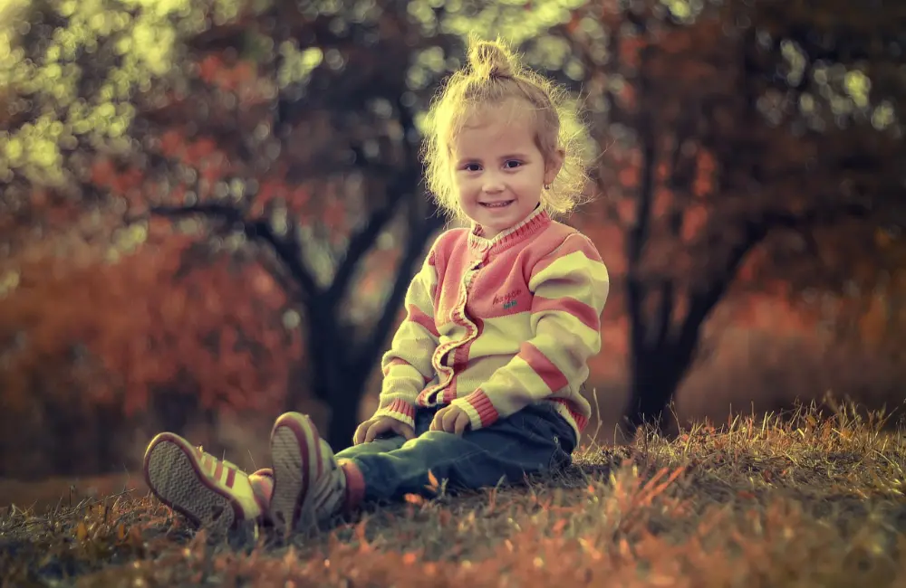 Bambina sorridente seduta sull'erba in un bosco autunnale